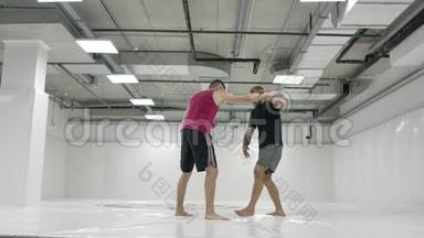 在一间白色的房间里，两个男摔跤手在扔垫子。 抓住一个抓斗把自己扔出去